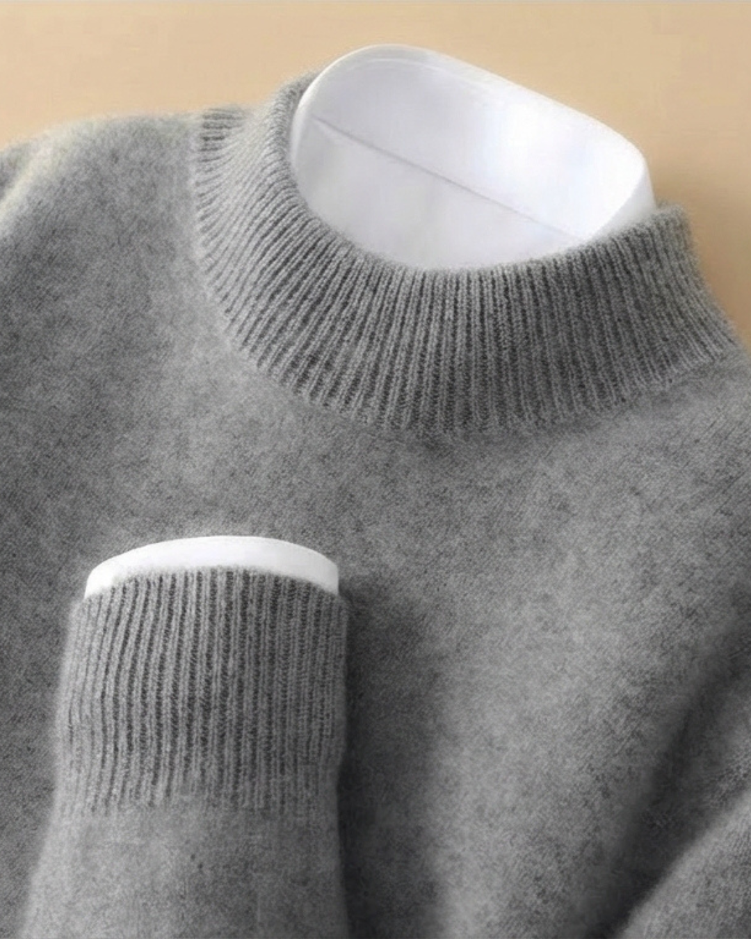 Jersey de punto gris con cuello alto de canalé y puños ribeteados en blanco.