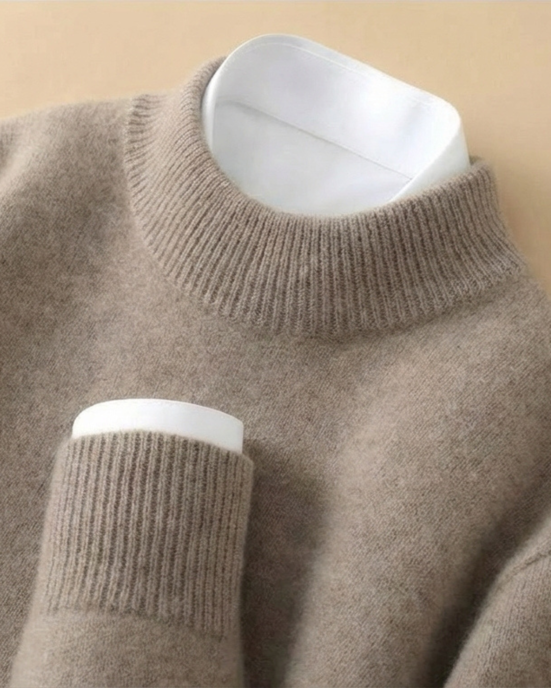 Jersey de punto beige con cuello alto de canalé y puño ribeteado blanco.